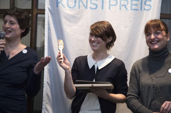 Die Gewinnerin des Hauptpreises, Diana Artus, mit einem von Künstlerin Barbara Duisberg gestalteten goldenen Pinsel bei der Verleihung neben Katharina Bieler, Leiterin des Fachbereichs Kultur des Bezirksamtes Neukölln (l.) und Anne Keilholz, Geschäftsführerin von STADT UND LAND